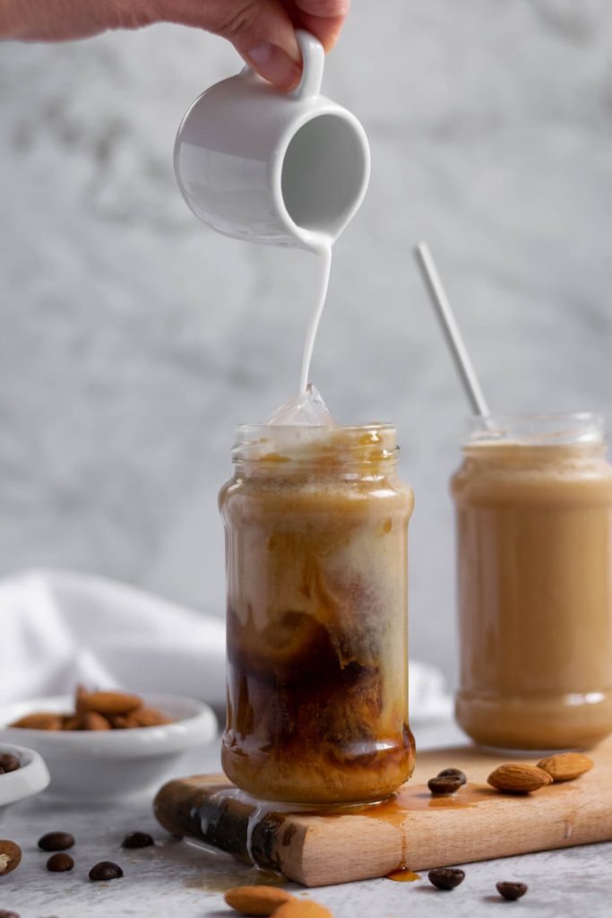 Pouring almond milk over iced coffee